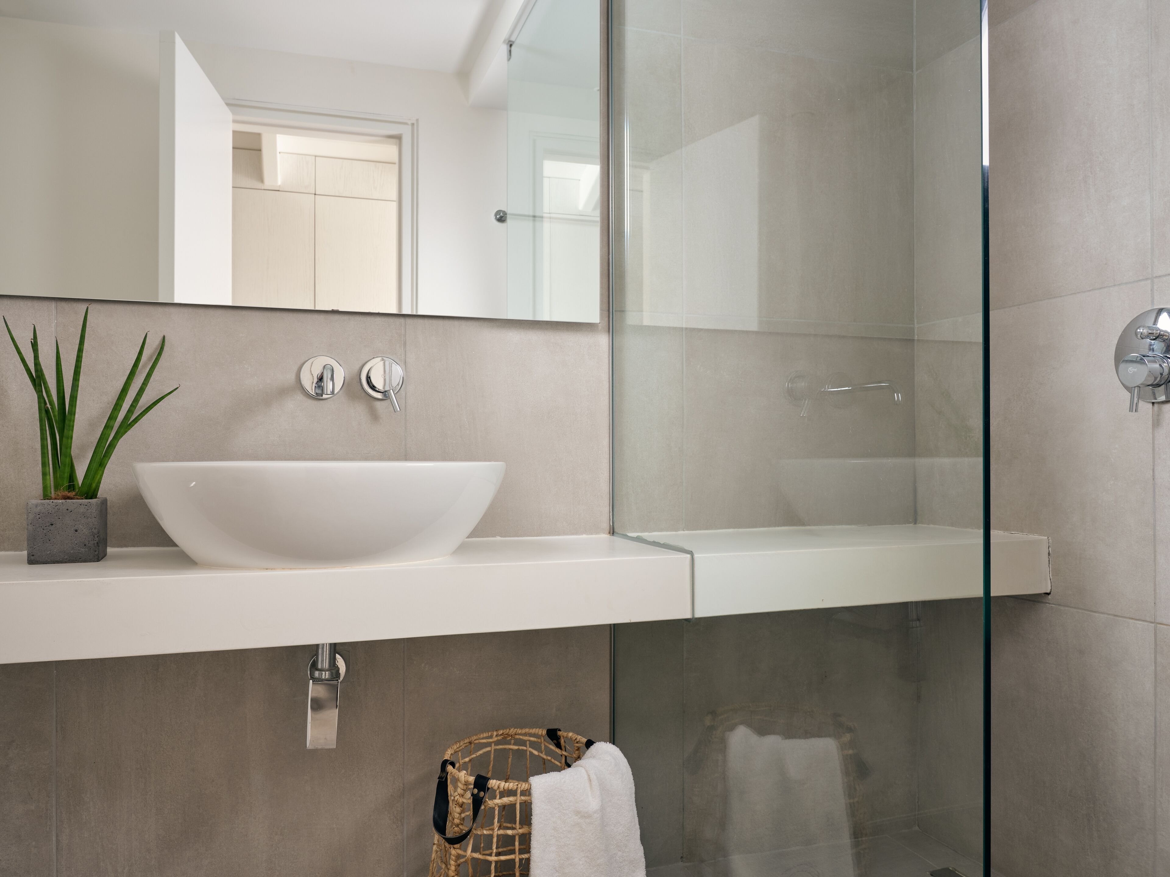 A modern bathroom with a white sink, a glass shower enclosure, and a potted plant.