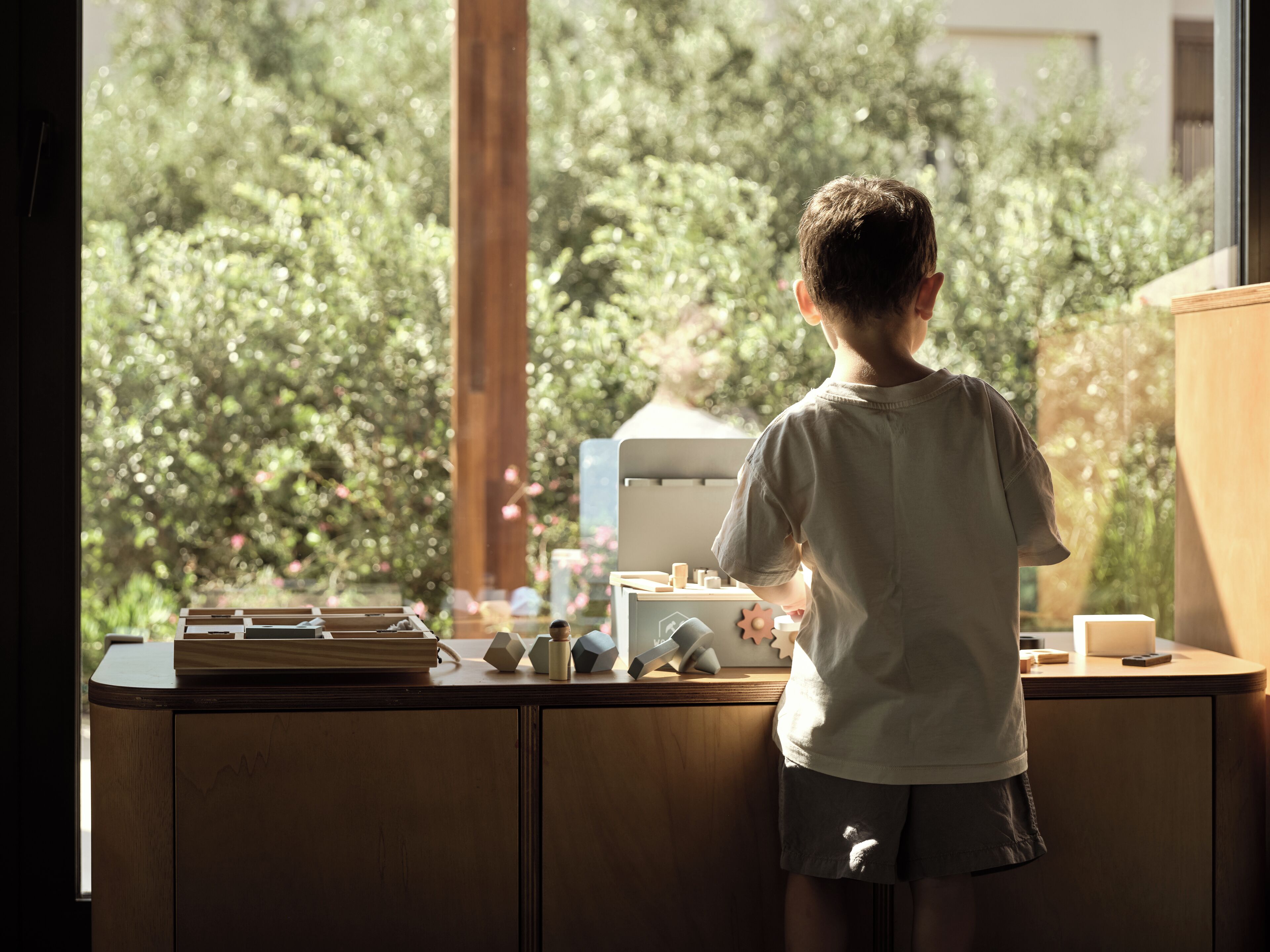 Niño de pie junto a una ventana con vistas a la vegetación.