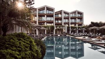 Ein modernes Hotel mit Pool, Liegestühlen und dem Gebäude, das sich im Wasser spiegelt.