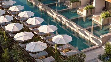 A pool area with multiple lounge chairs and umbrellas, surrounded by greenery and steps leading to a building.