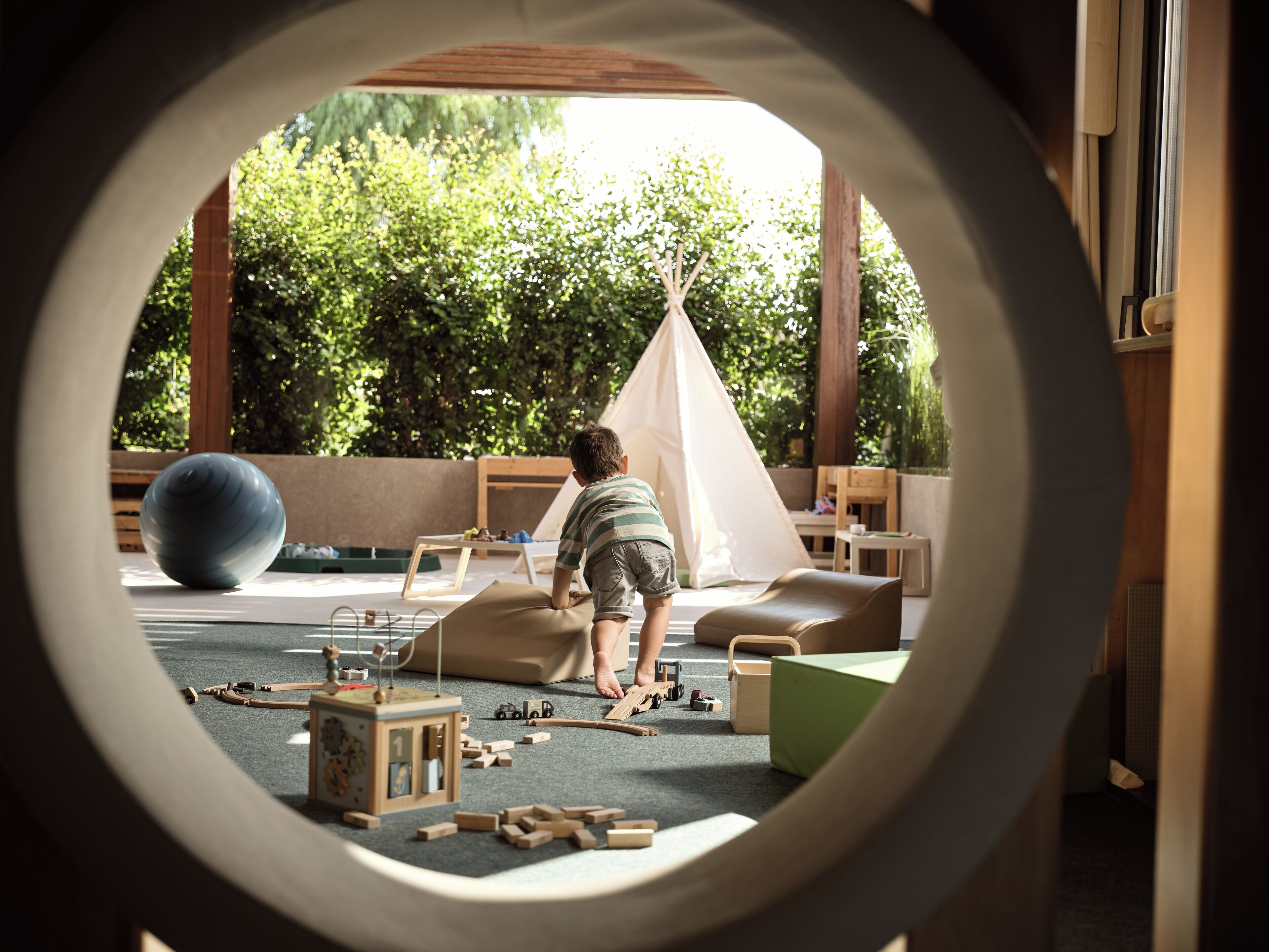 A child playing in a play area with a tent, toys, and a large ball.