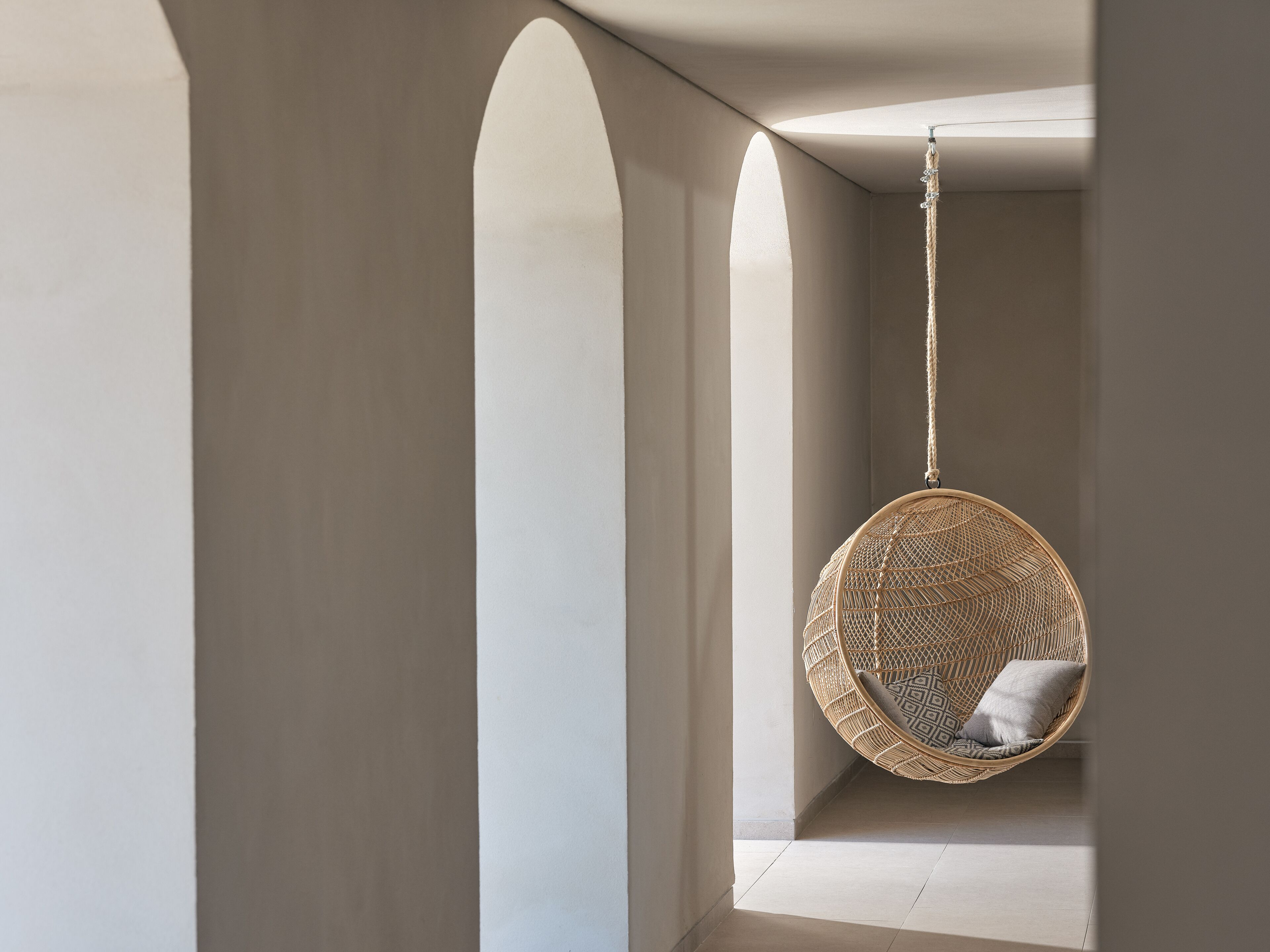A modern interior with a hanging rattan chair and a view through an arched doorway.