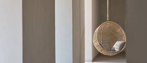 A modern interior with a hanging rattan chair and a view through an arched doorway.