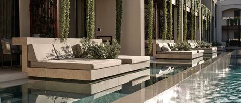 A poolside area with a long, narrow pool, a beige sofa, and a chair.