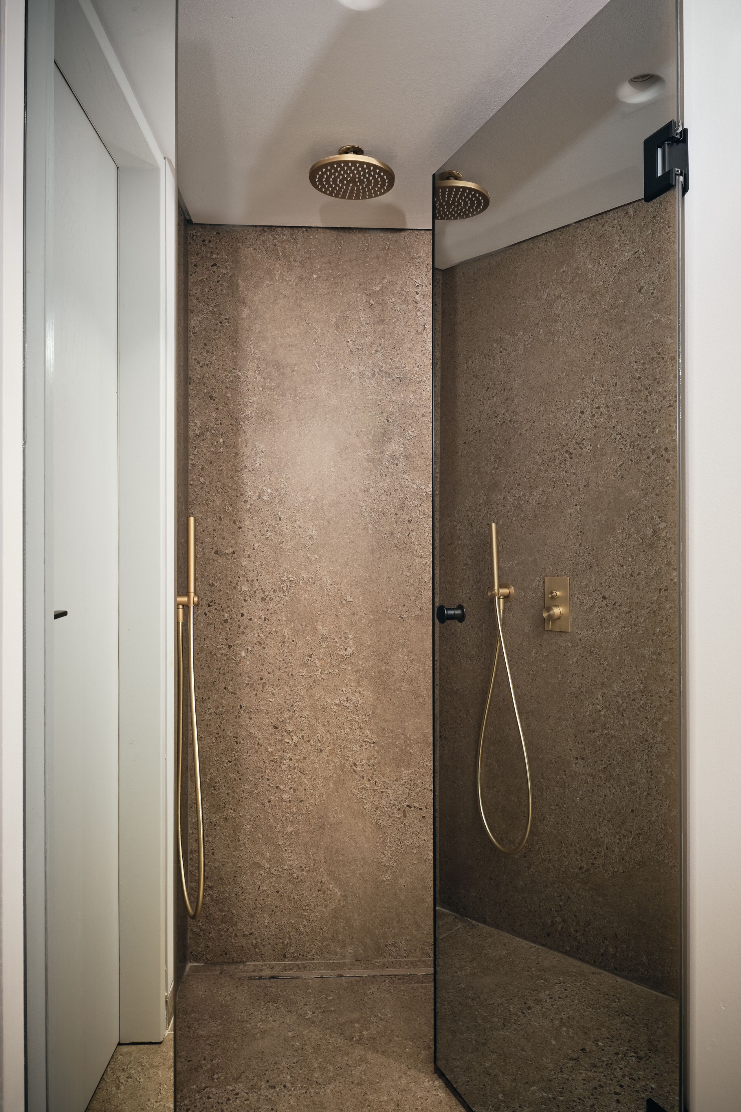 Une douche moderne dotée d’une paroi en verre, d’un mur à texture et d’un pommeau de douche doré.