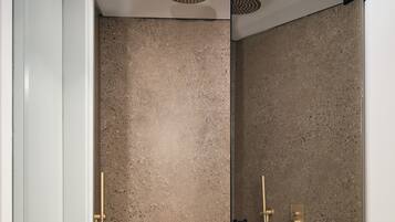 Une douche moderne dotée d’une paroi en verre, d’un mur à texture et d’un pommeau de douche doré.