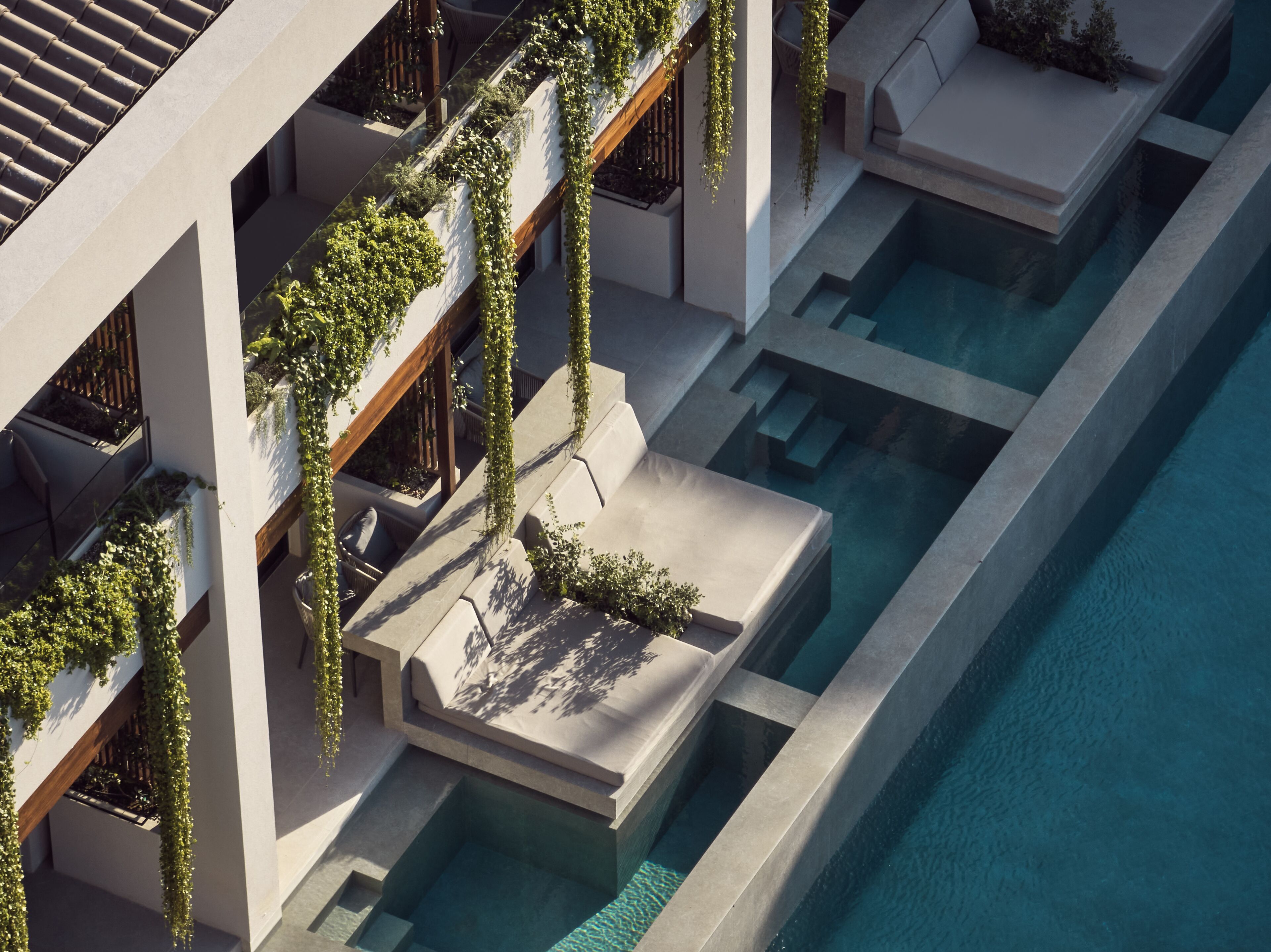Un hotel moderno con piscina en la azotea, zonas de estar al aire libre y abundante vegetación.
