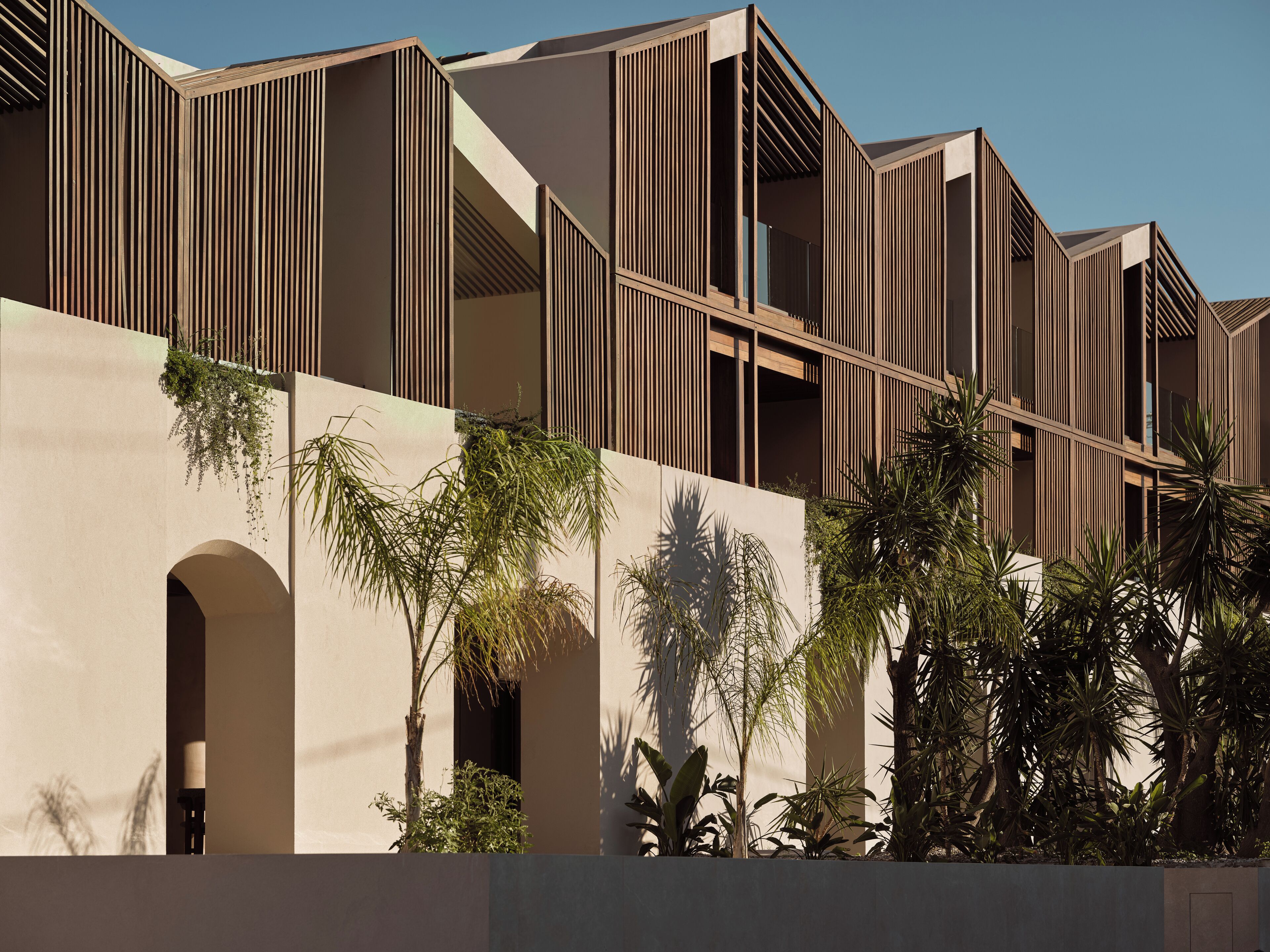 Un edificio moderno con una facciata geometrica, numerosi balconi e vegetazione lussureggiante antistante.
