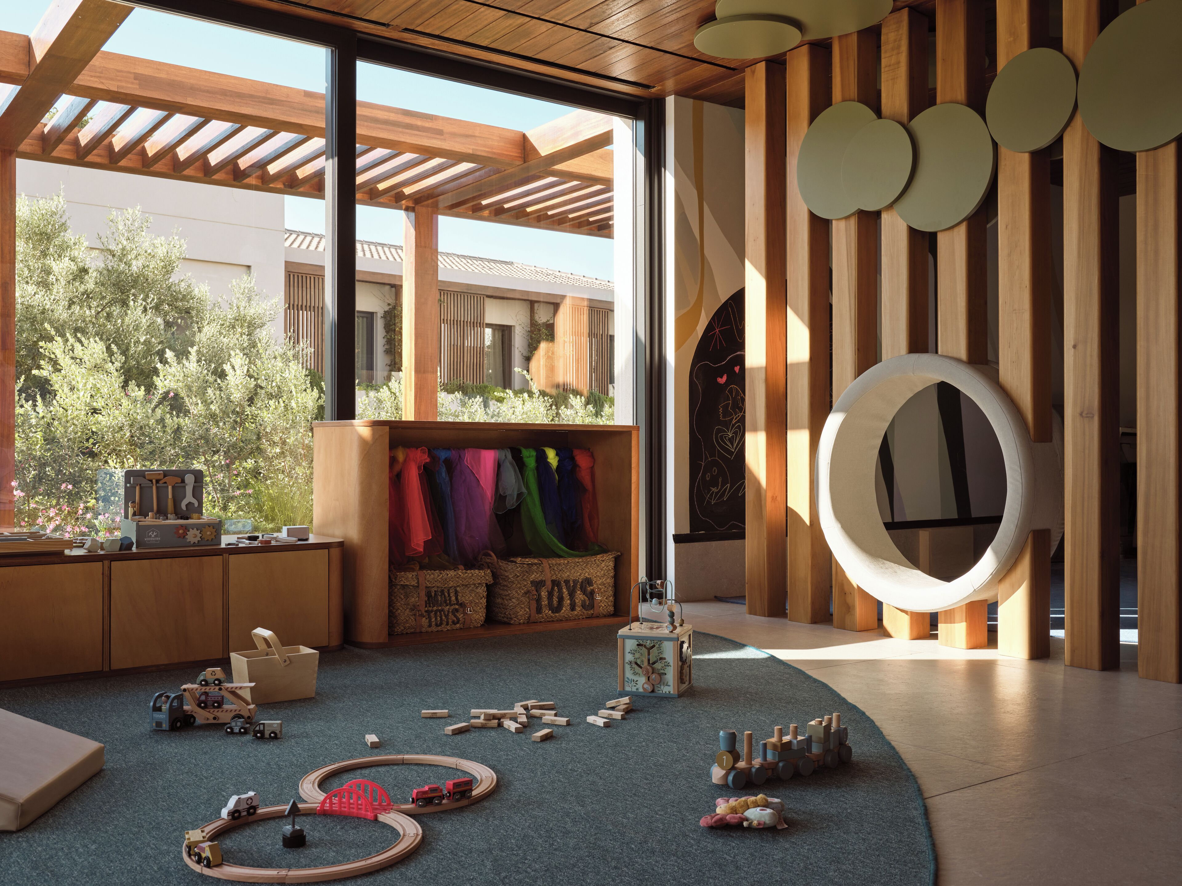 A modern interior with a wooden play area, a large window, and a circular wall decoration.
