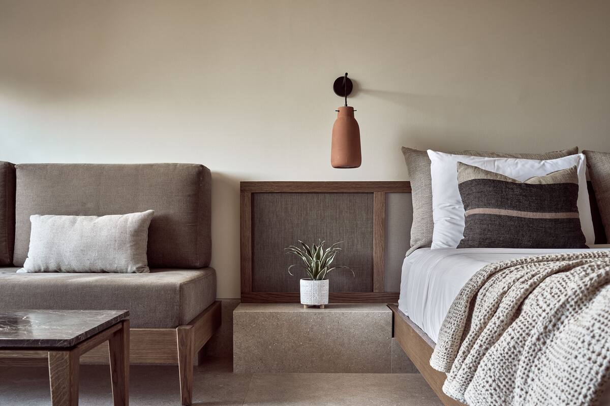 Et hyggeligt værelse med sofa, et lille bord, et natbord med en plante og en seng med pude med striber.