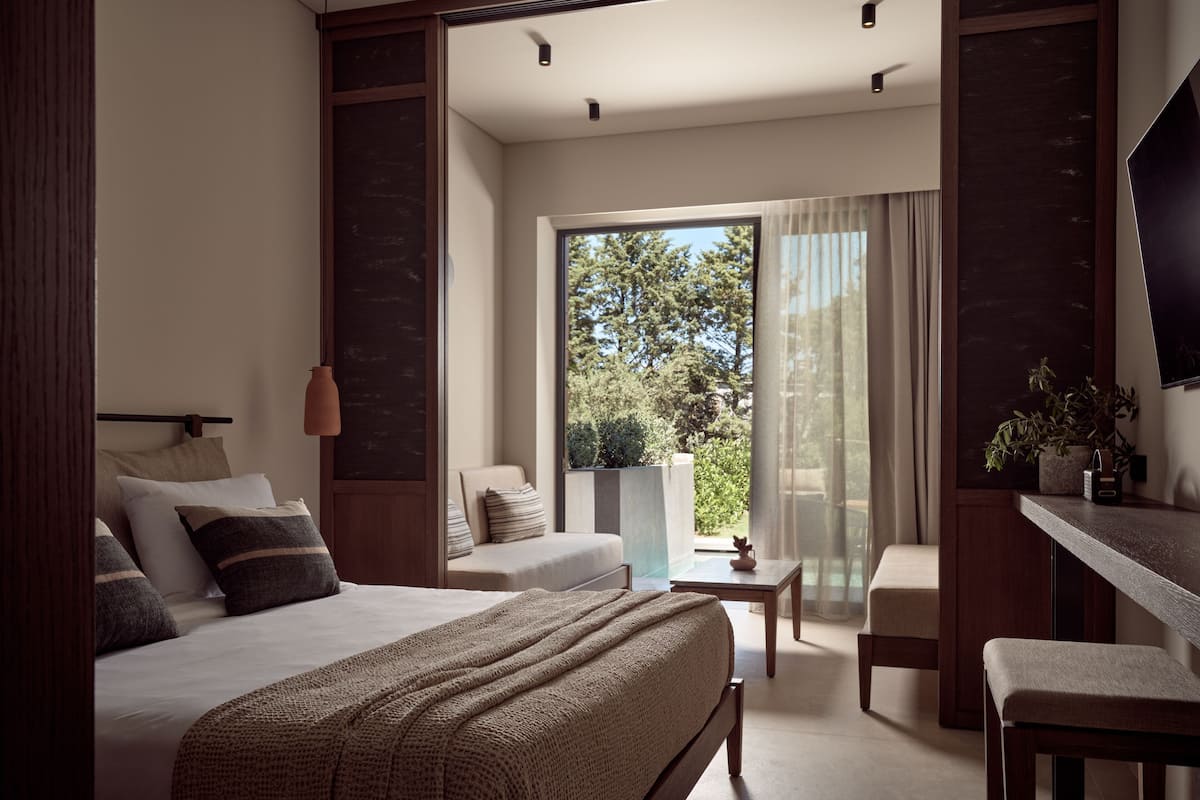 Et moderne hotelværelse med en stor seng, en sofa, et skrivebord og en balkon med udsigt til træer.