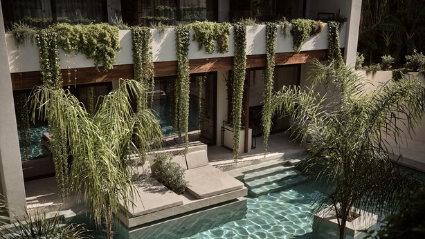 Un área de piscina moderna con agua cristalina, rodeada de follaje y asientos de piedra.