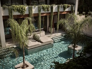 Un área de piscina moderna con agua cristalina, rodeada de follaje y asientos de piedra.