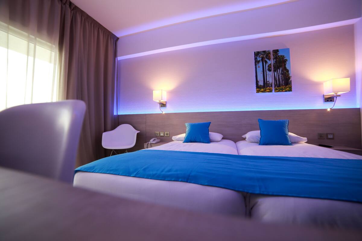 Una habitación de hotel moderna con una cama grande, dos lámparas de noche, una mesita de noche y una silla.