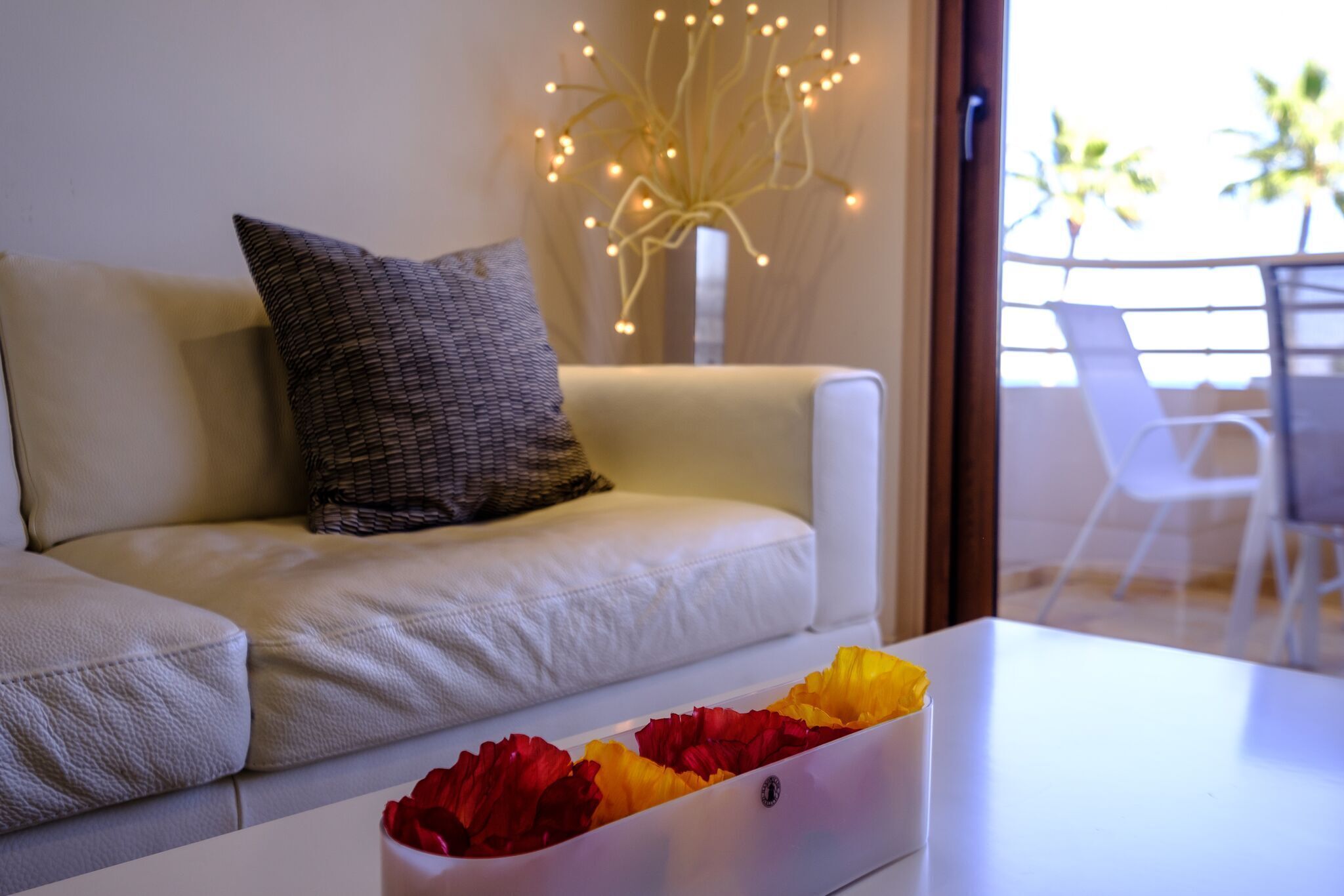 A modern living room with a white sofa, a decorative vase with lights, and a table with a flower arrangement.