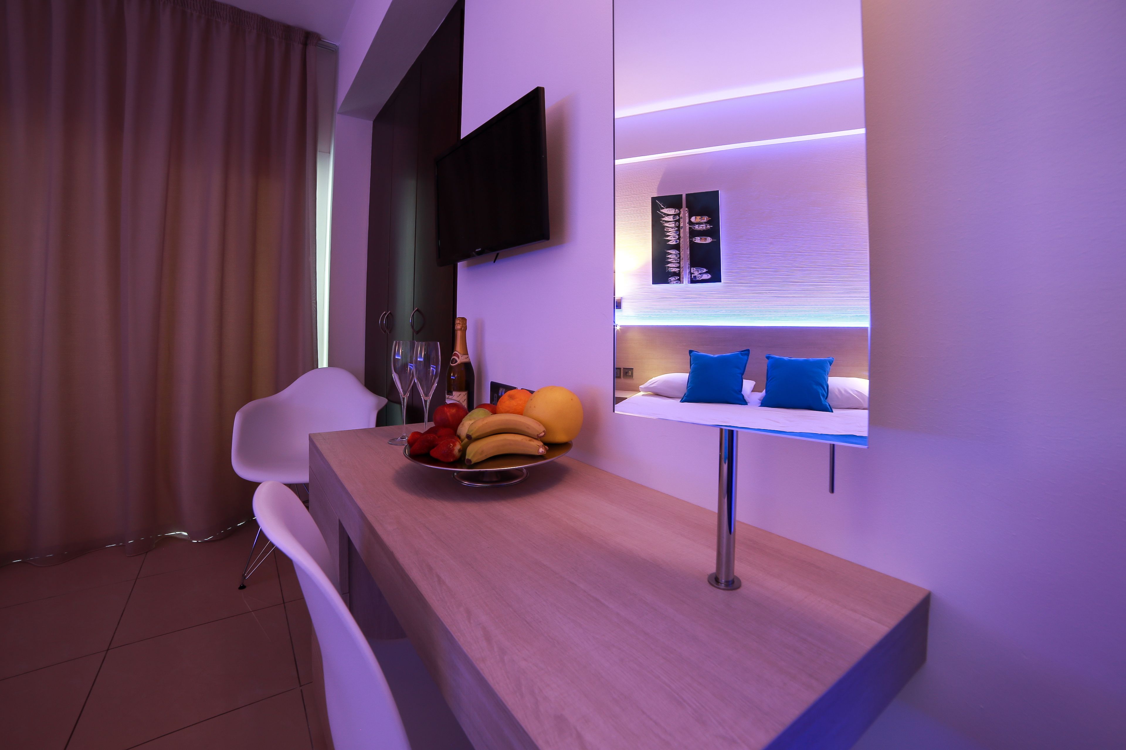 A modern hotel room with a wooden bar, a flat-screen TV, and a fruit bowl.