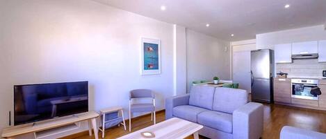 Una sala de estar moderna con un televisor de pantalla plana, un sofá, una mesa de centro y una mesita auxiliar.