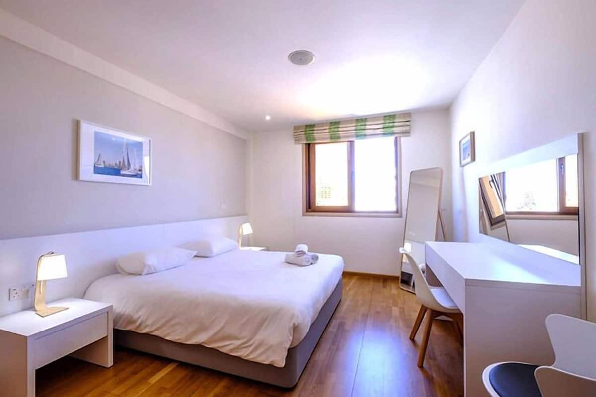 Un dormitorio con cama, mesitas de noche, escritorio y una silla.