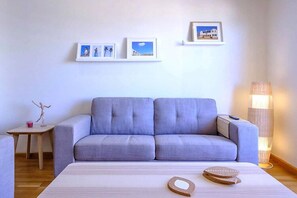 A modern living room with a grey sofa, a wooden coffee table, and a floor lamp. There are framed pictures on the wall.