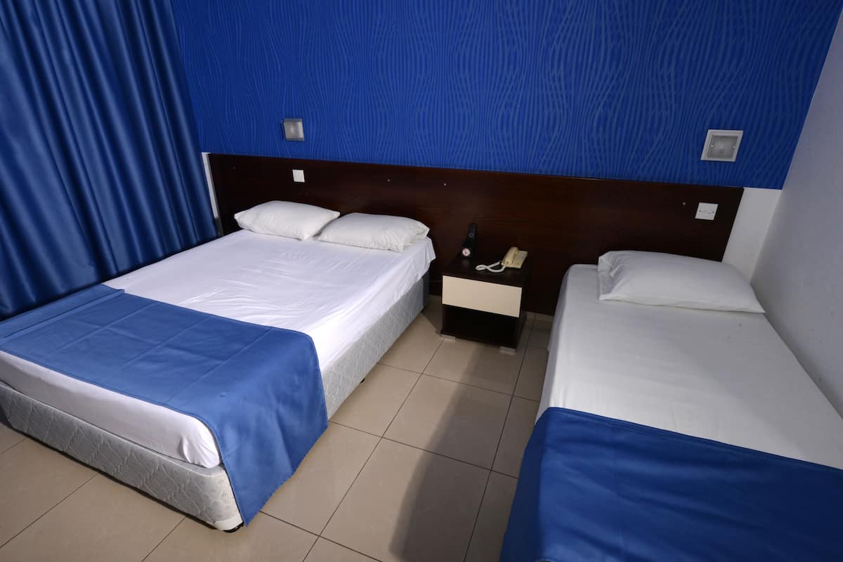 Una habitación de hotel con dos camas, una mesita de noche y un teléfono, además de una cortina azul.