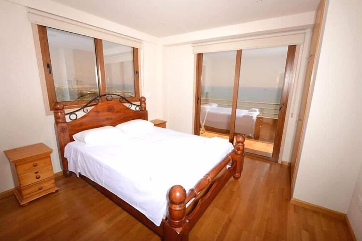 Un dormitorio con una cama de madera, una mesita de noche, un ventanal y un balcón con vistas.