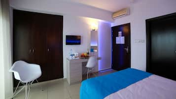 A hotel room with a bed, a desk, a chair, a wardrobe, a TV, and a door with a lock.