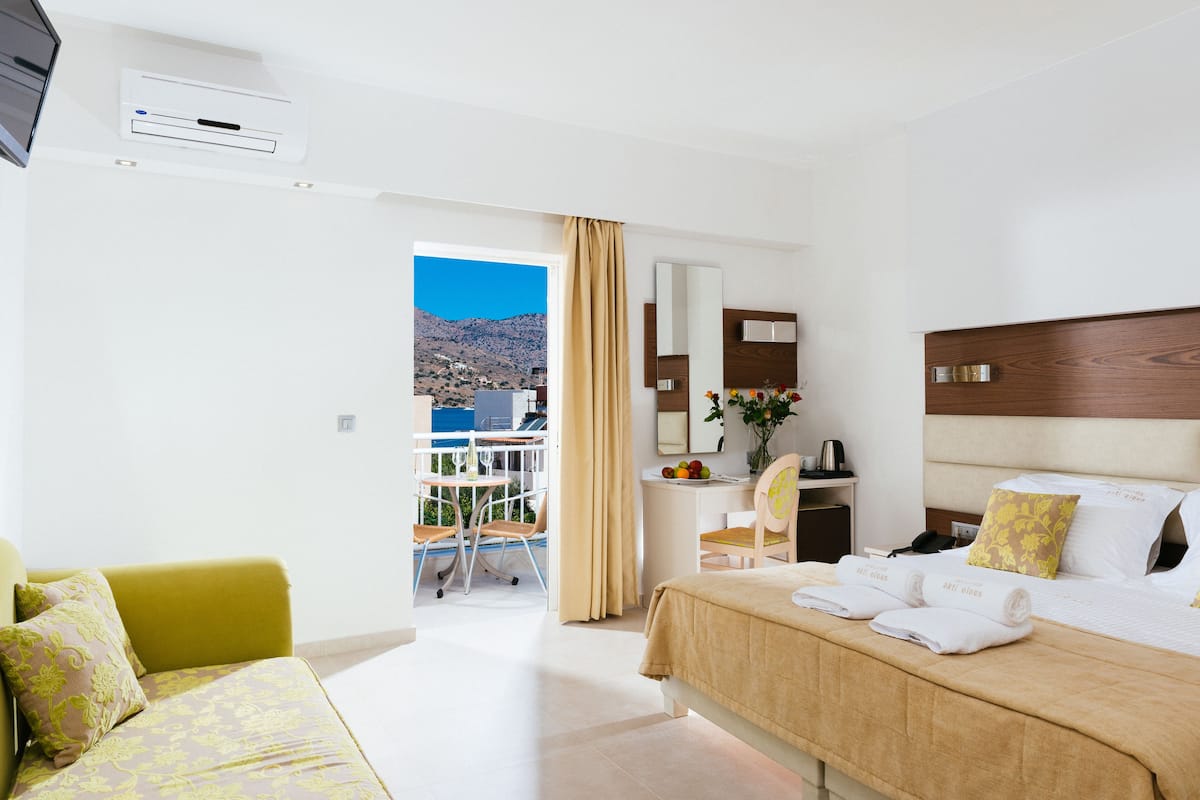 A hotel room with a bed, a desk, a chair, a balcony with a view of the mountains, and a TV.