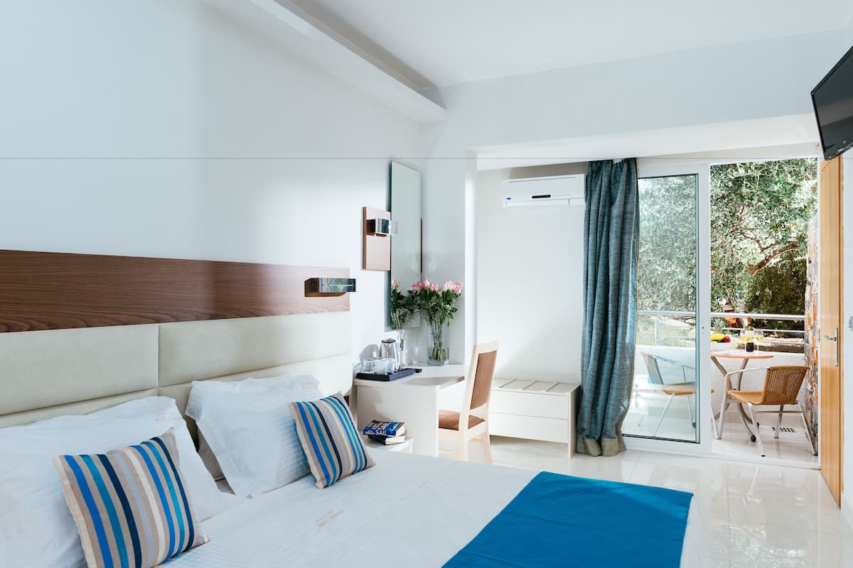 A modern hotel room with a large bed, a desk, and a balcony with a view of the outdoors.