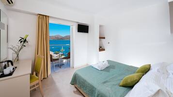 A hotel room with a bed, a desk with a chair, a TV, and a view of the sea.