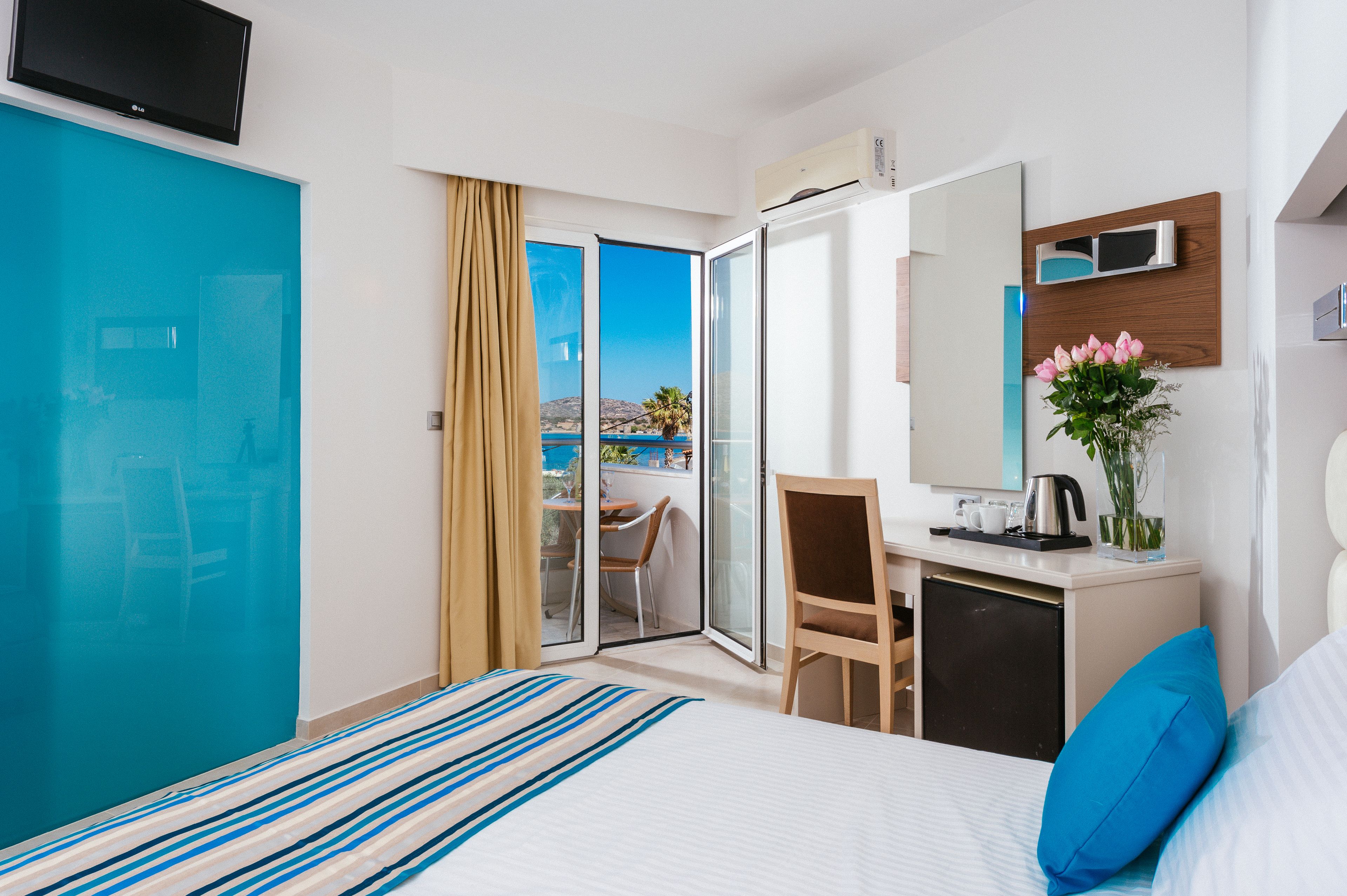 A hotel room with a bed, a desk, a chair, a TV, a minibar, and a view of the outdoors.