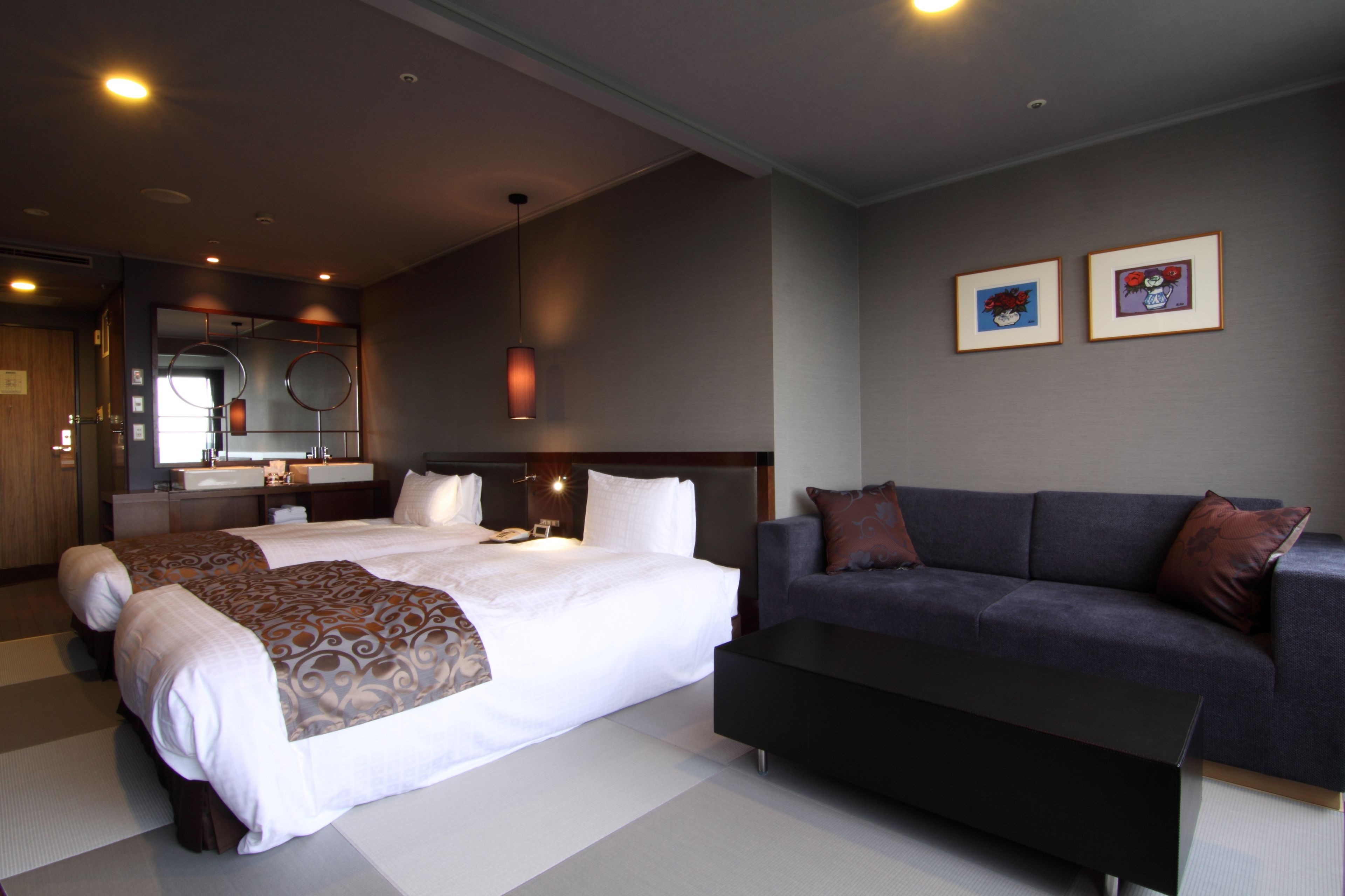 A hotel room with two beds, a sofa, a large mirror, and framed artwork on the wall.