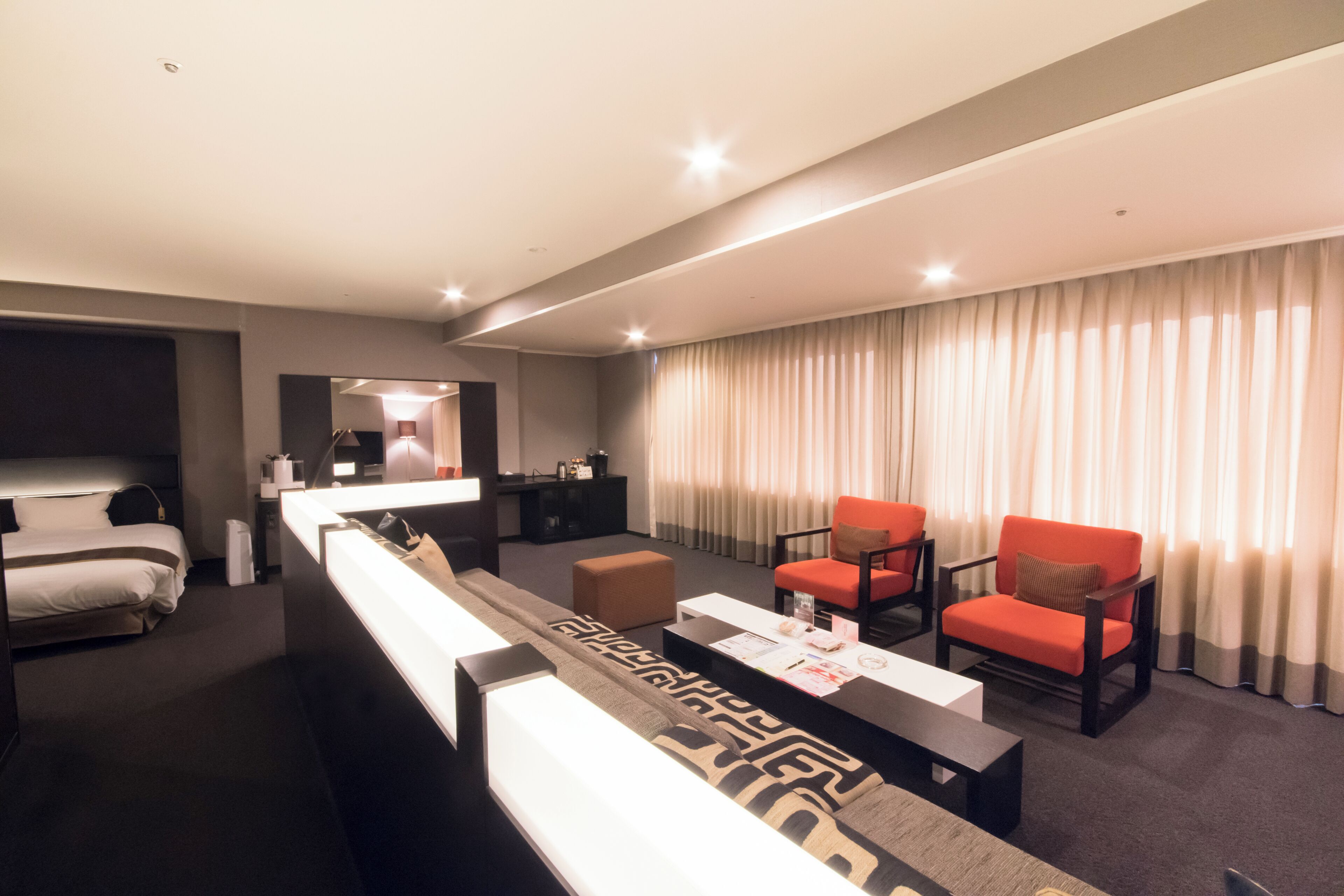 A hotel room with a bed, a sofa, a coffee table, and two armchairs.