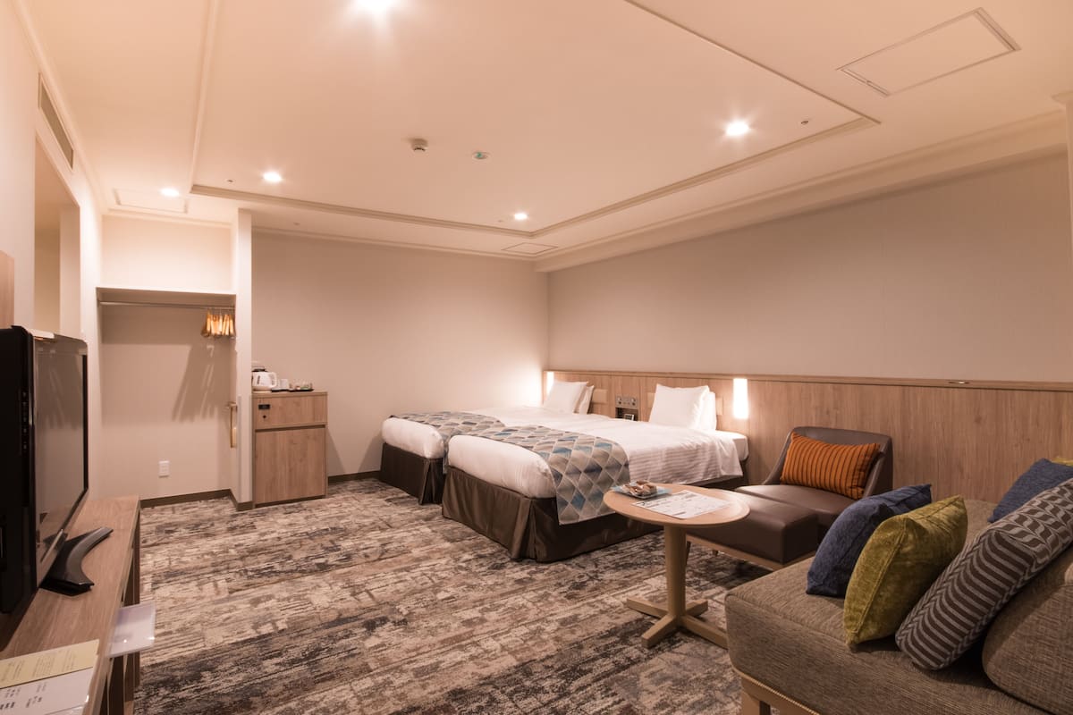 A hotel room with two beds, a sofa, a small table, and a TV.