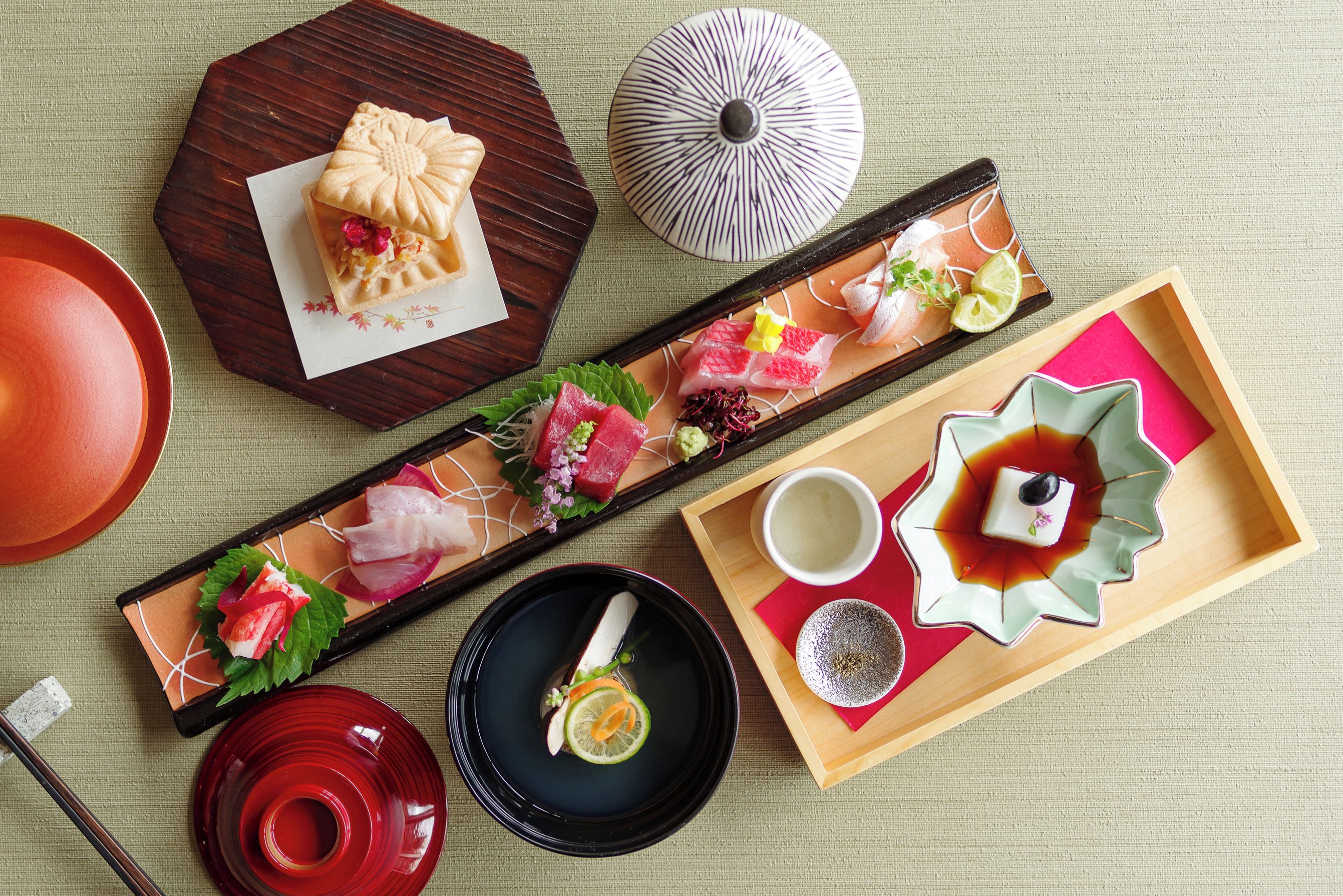A traditional Japanese meal with sashimi, a small cake, and a bowl of soup.
