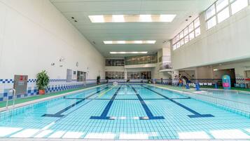 An indoor swimming pool with clear lane markings, a tiled floor, and a high ceiling with skylights.