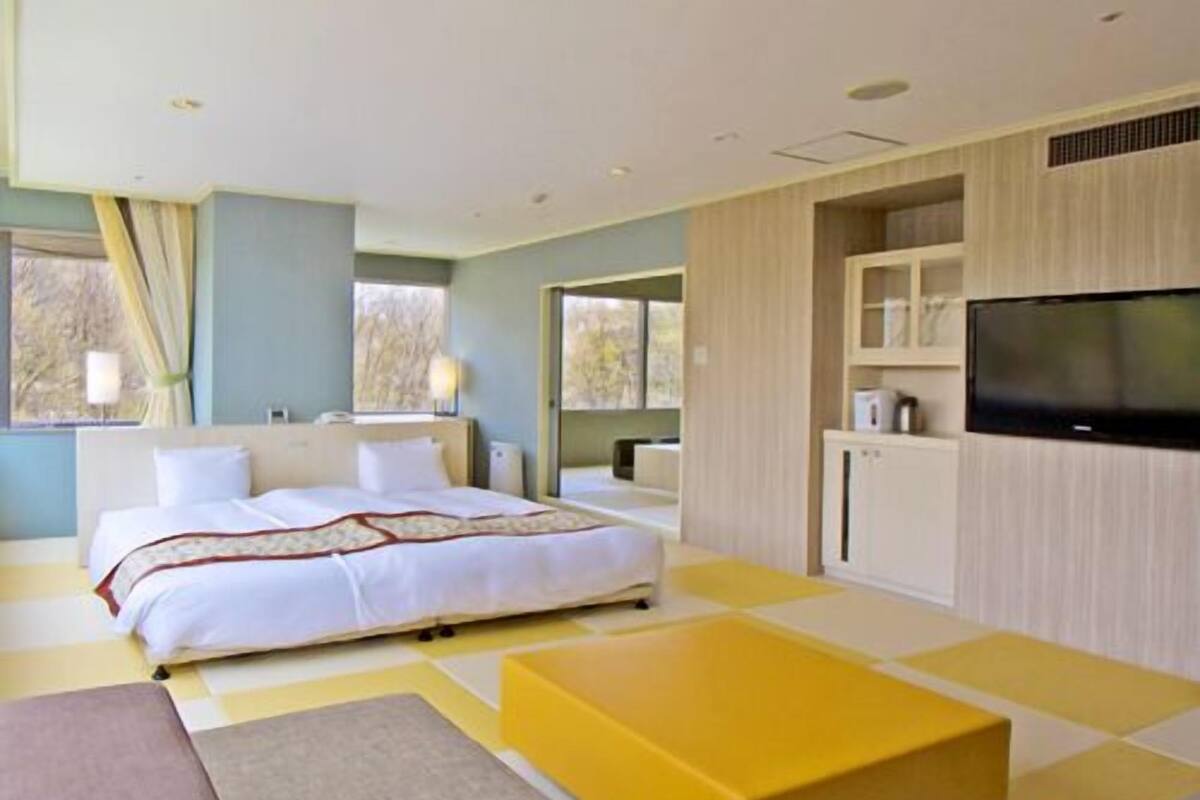 A modern hotel room with a bed, a flat-screen TV, a sofa, and a coffee table.