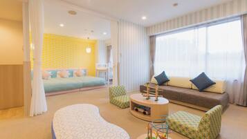 Quarto de hotel com cama, sofá, área de recreação e uma grande janela.