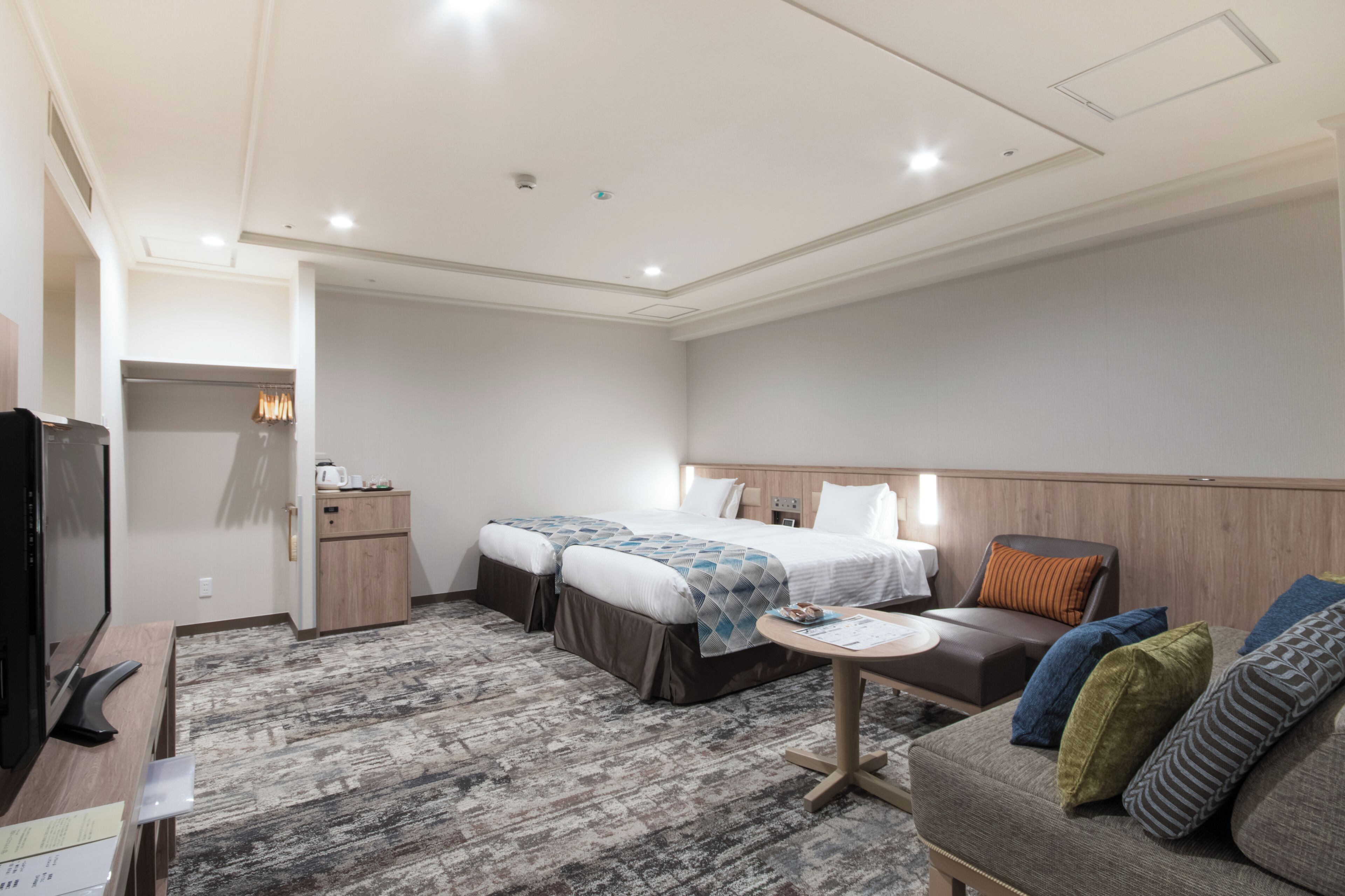 A hotel room with a bed, two bedside tables, a sofa, a small table, and a television.
