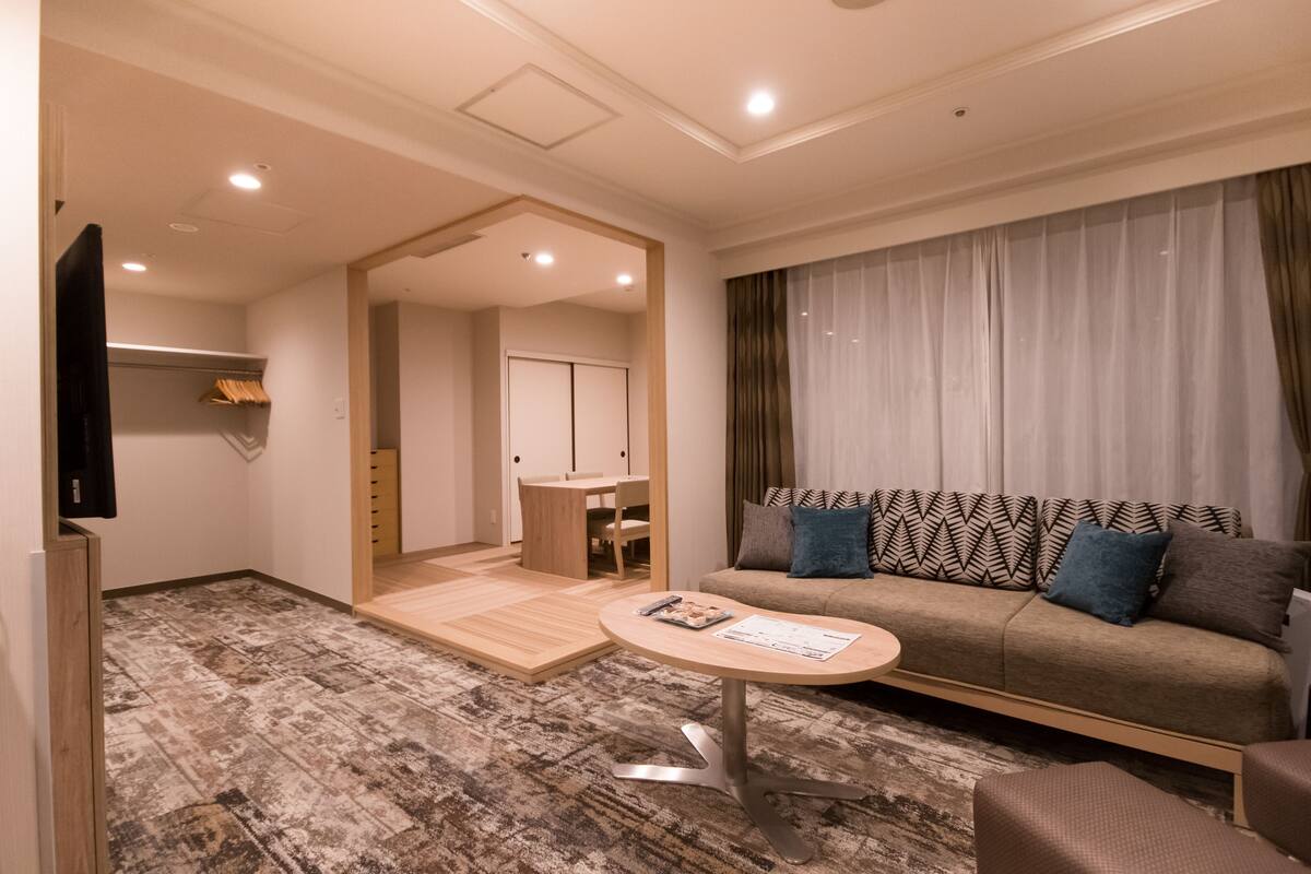 A modern hotel room with a sofa, a small table, a TV, and a wooden floor.