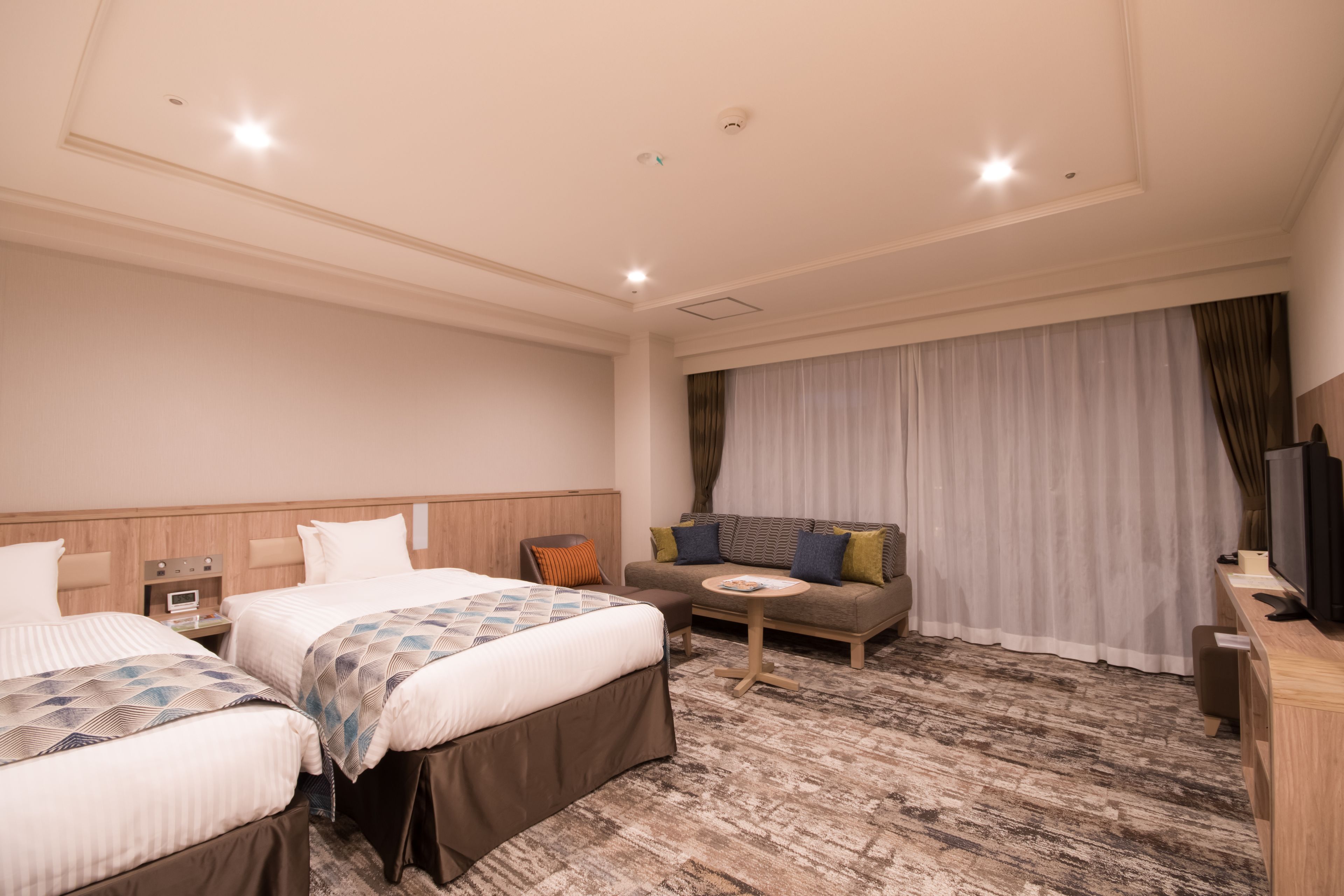 Camera d'hotel con due letti, un divano, un tavolino, una TV e un'ampia finestra con tende.