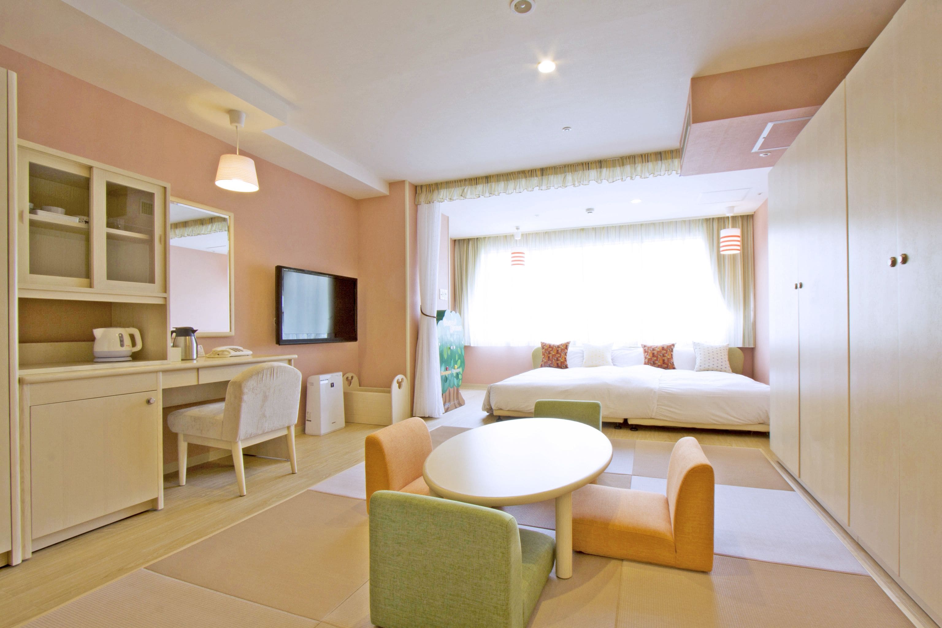A hotel room with a bed, a desk with a chair, a television, and a window with curtains.