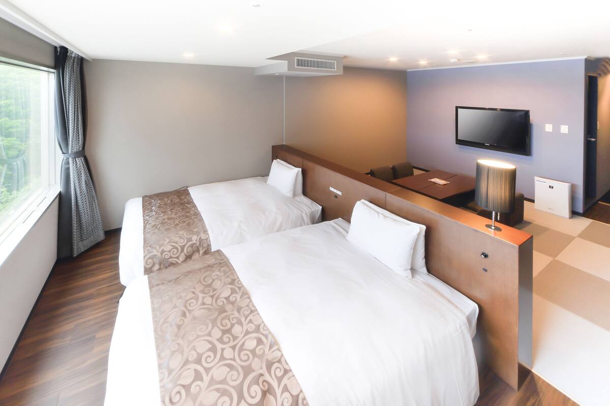 A hotel room with two beds, a TV, a desk, and a window with curtains.