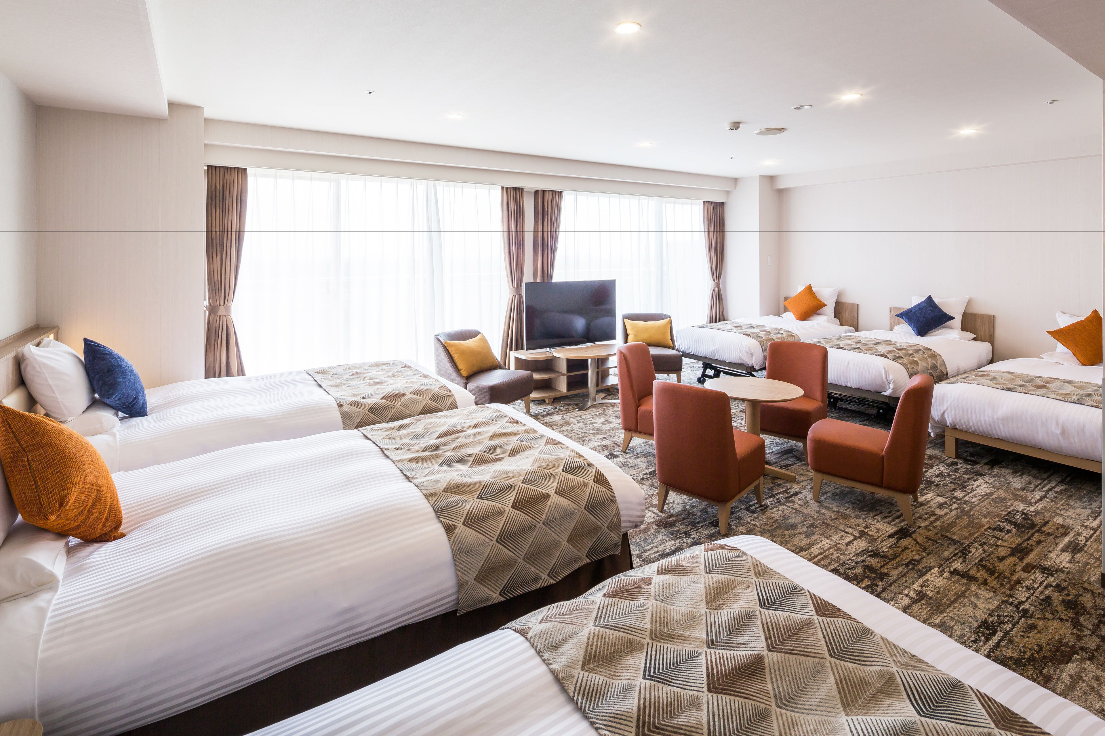 A hotel room with three beds, a TV, a small table, and a sofa.
