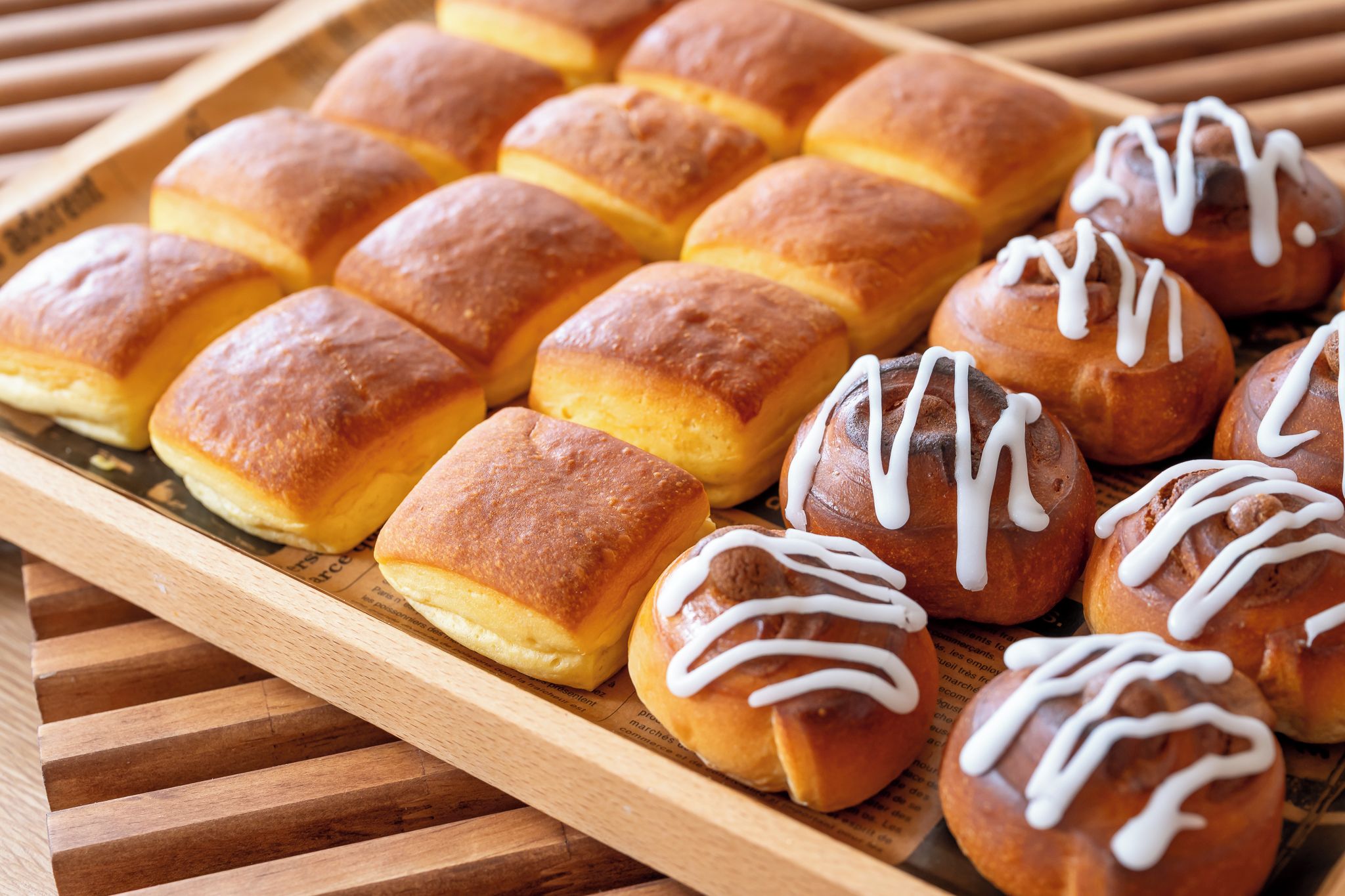 A tray of freshly baked rolls, some plain and others topped with white icing.