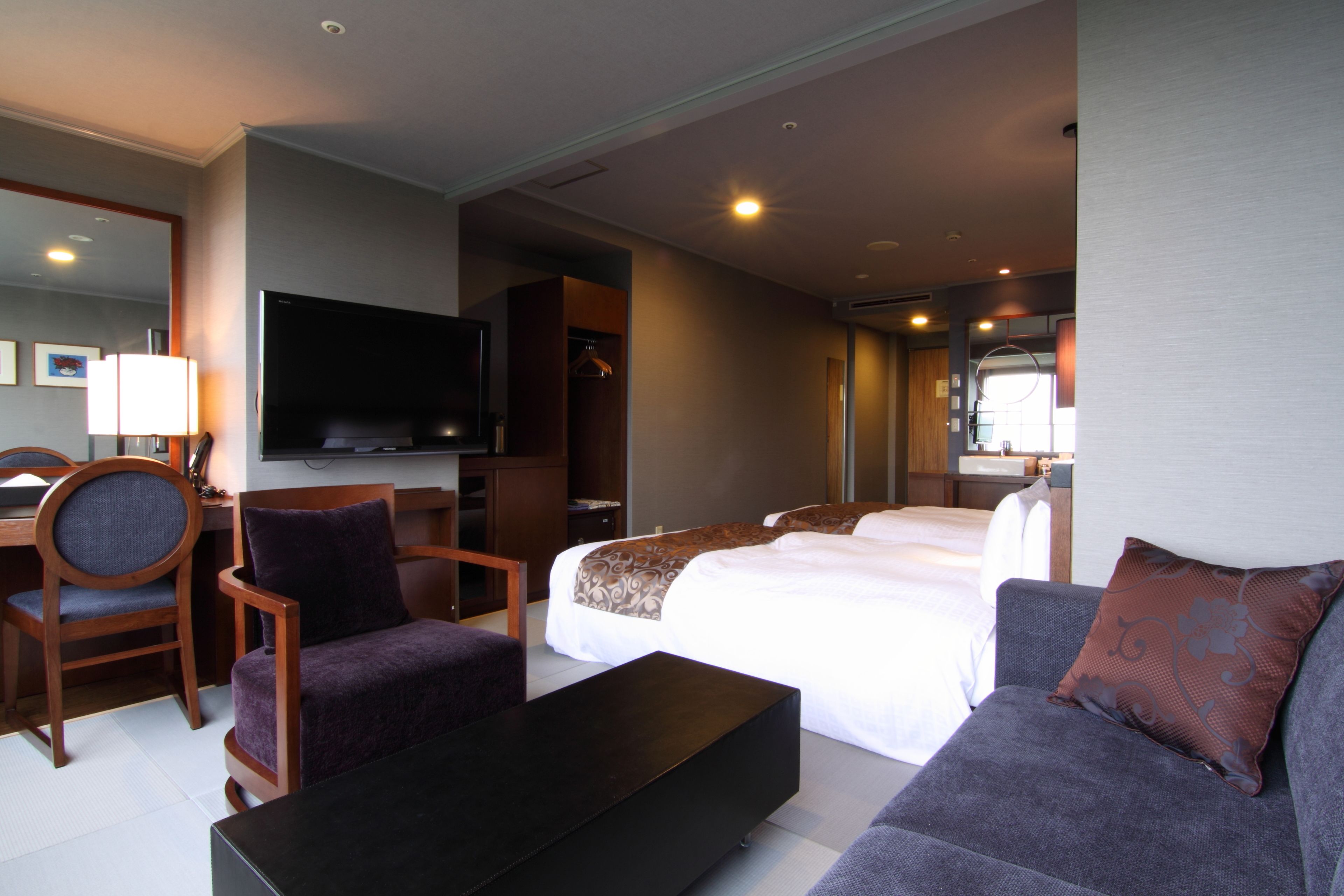A hotel room with a large bed, a sofa, a TV, and a desk with a chair.