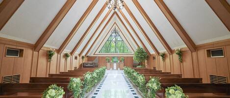A church interior with wooden pews, a central aisle, and a stained glass window.