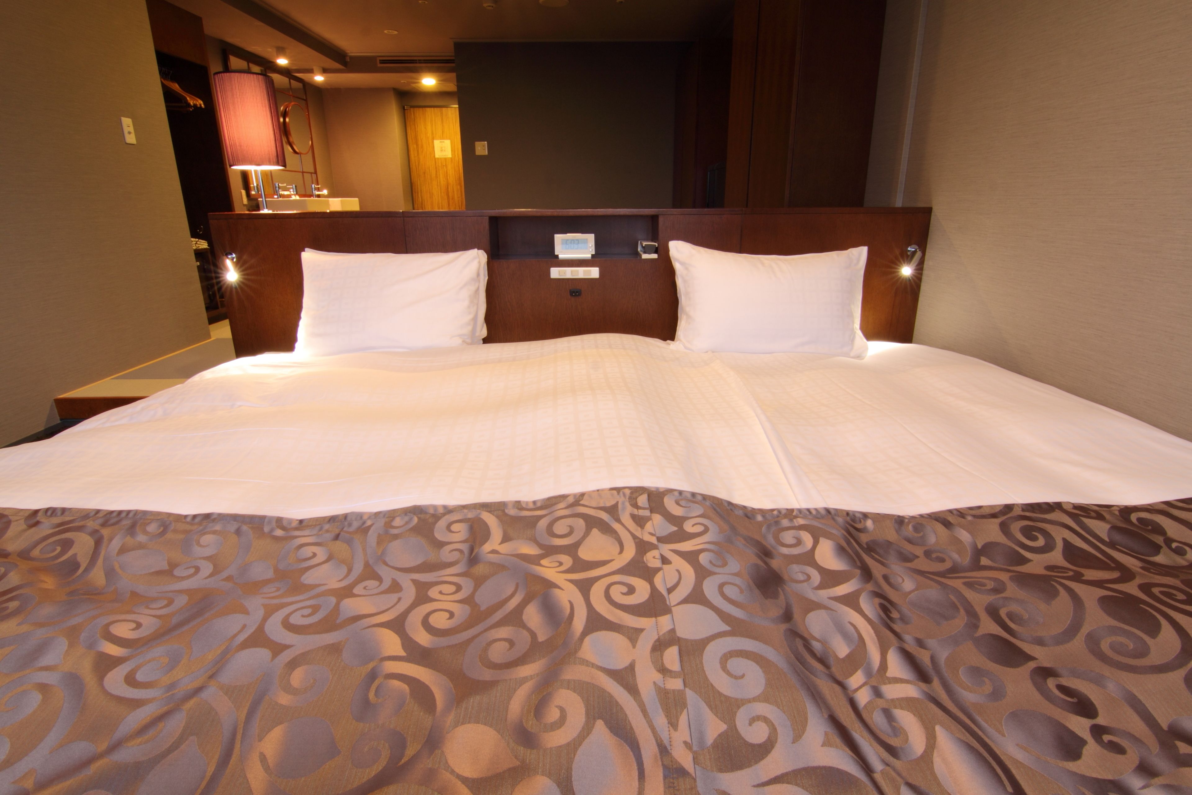 Una habitación de hotel con una cama grande, cabecera de madera, mesita de noche y un espejo.