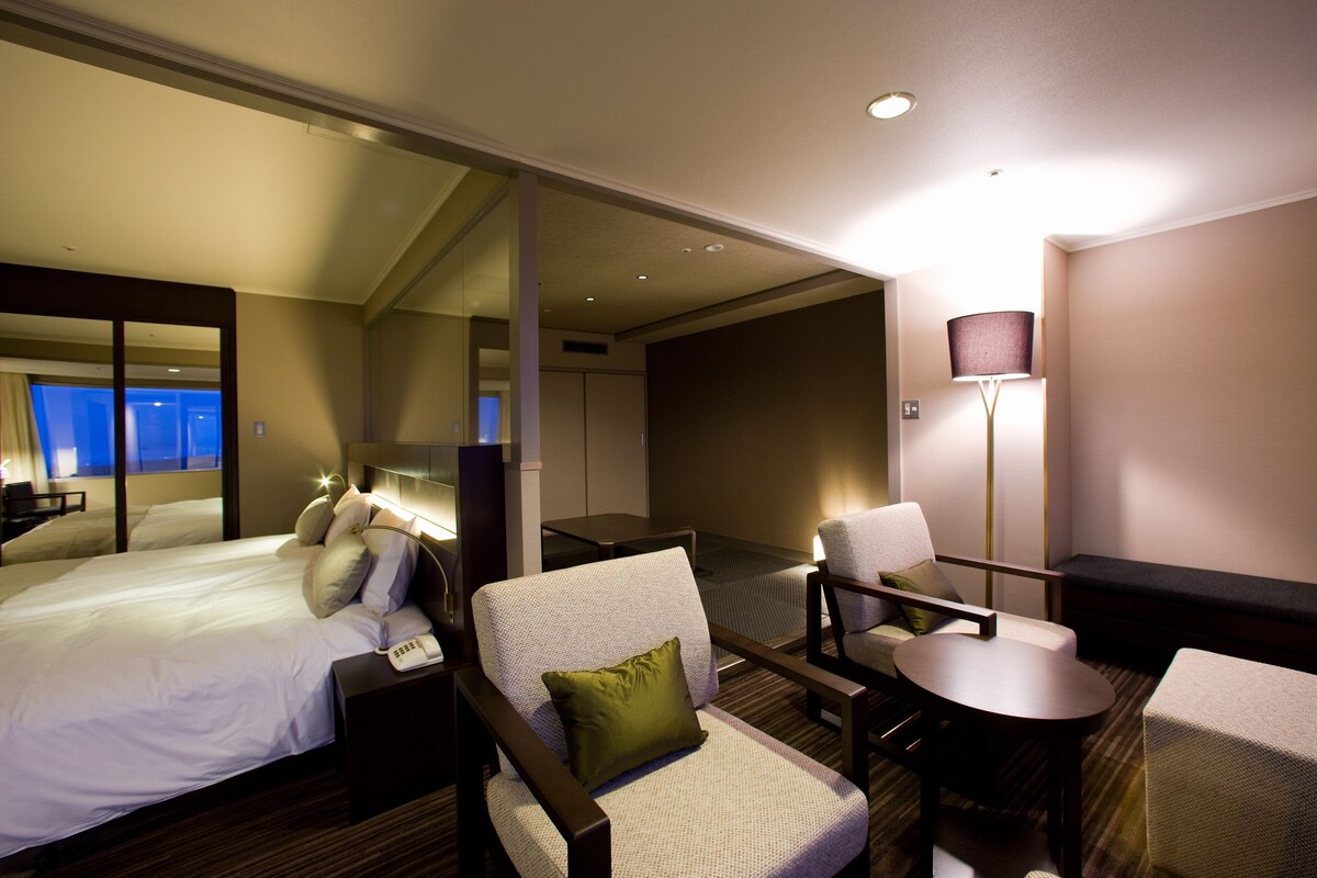 A hotel room with a bed, a desk, a chair, a sofa, and a lamp.