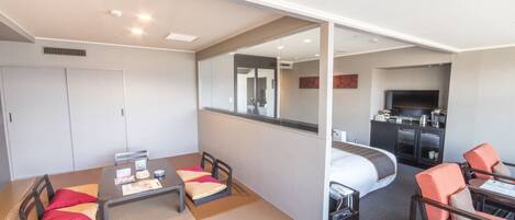 A hotel room with a dining table, chairs, a sofa, a bed, a TV, and a kitchenette.
