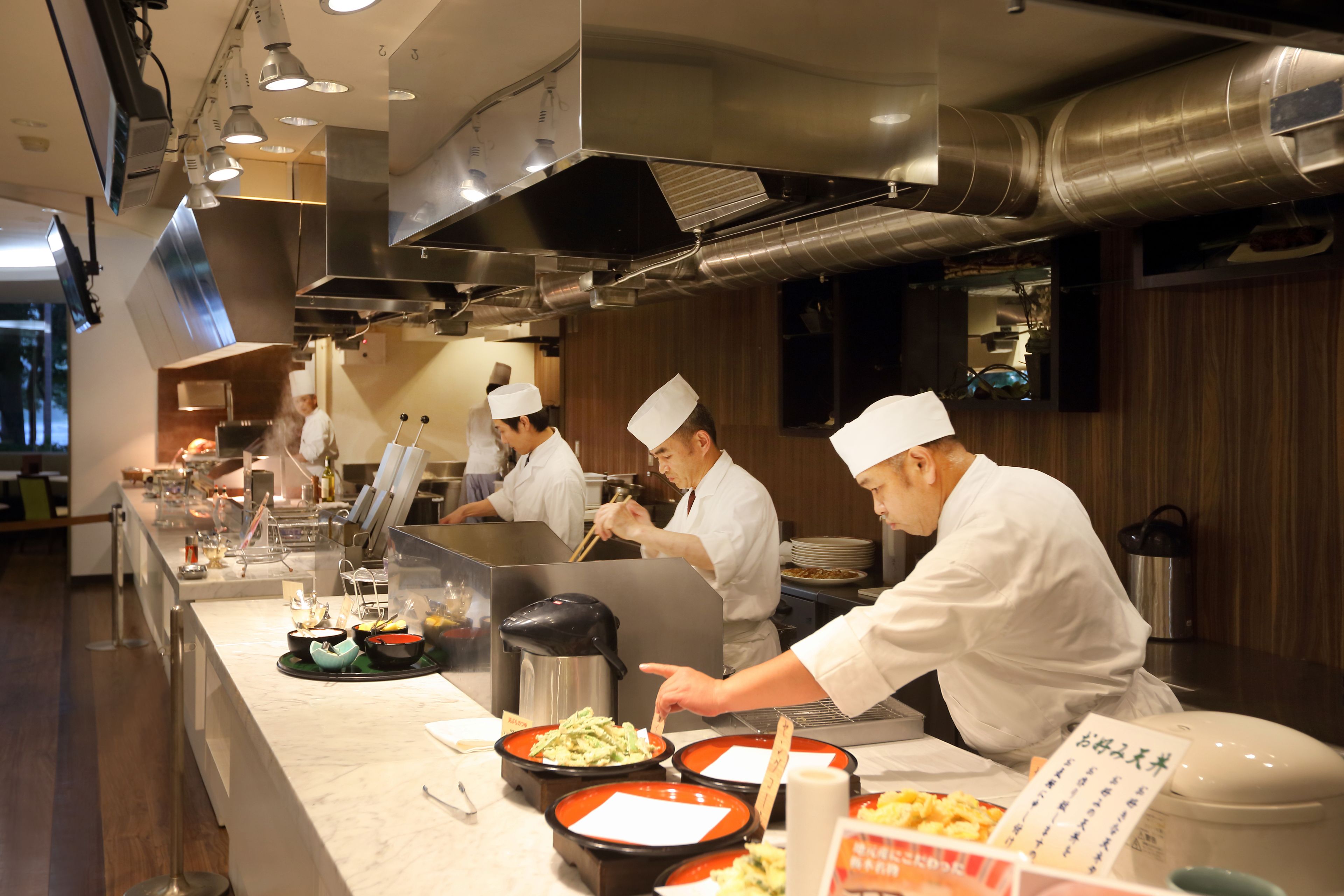 A professional kitchen with chefs preparing food, stainless steel appliances, and a marble countertop.